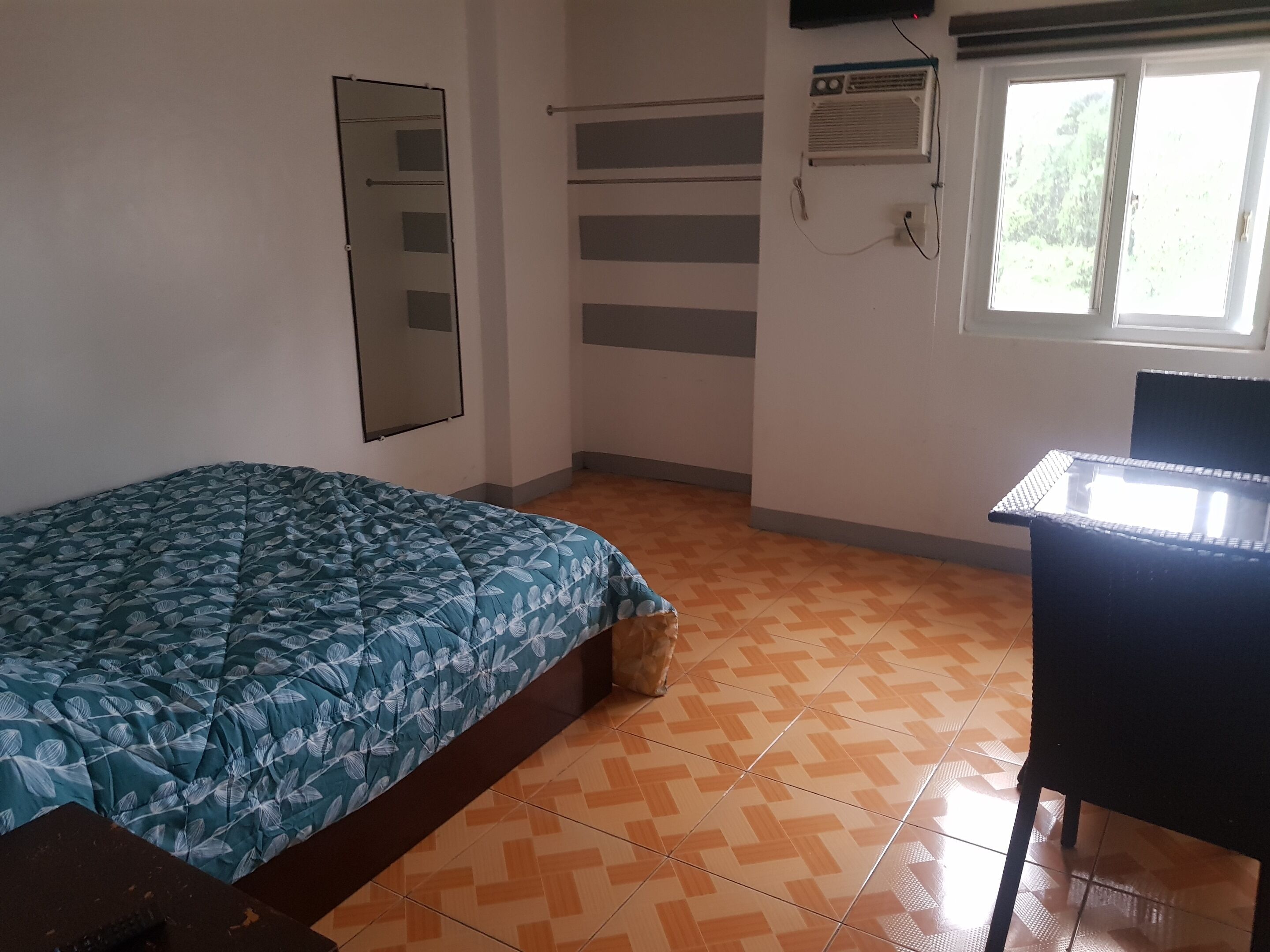 A bedroom with a bed, a desk, a mirror, and a window.