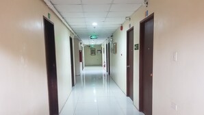 Un long couloir étroit, avec des portes de chaque côté, un sol carrelé et un plafond doté d’un éclairage encastré.