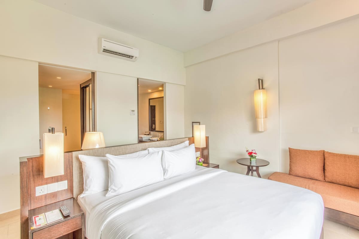 Een hotelkamer met een groot bed, een bank, een tafeltje met een lamp en een spiegel.