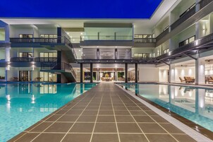 Interior de un hotel moderno con una piscina central, varios balcones y una escalera que lleva a pisos superiores.