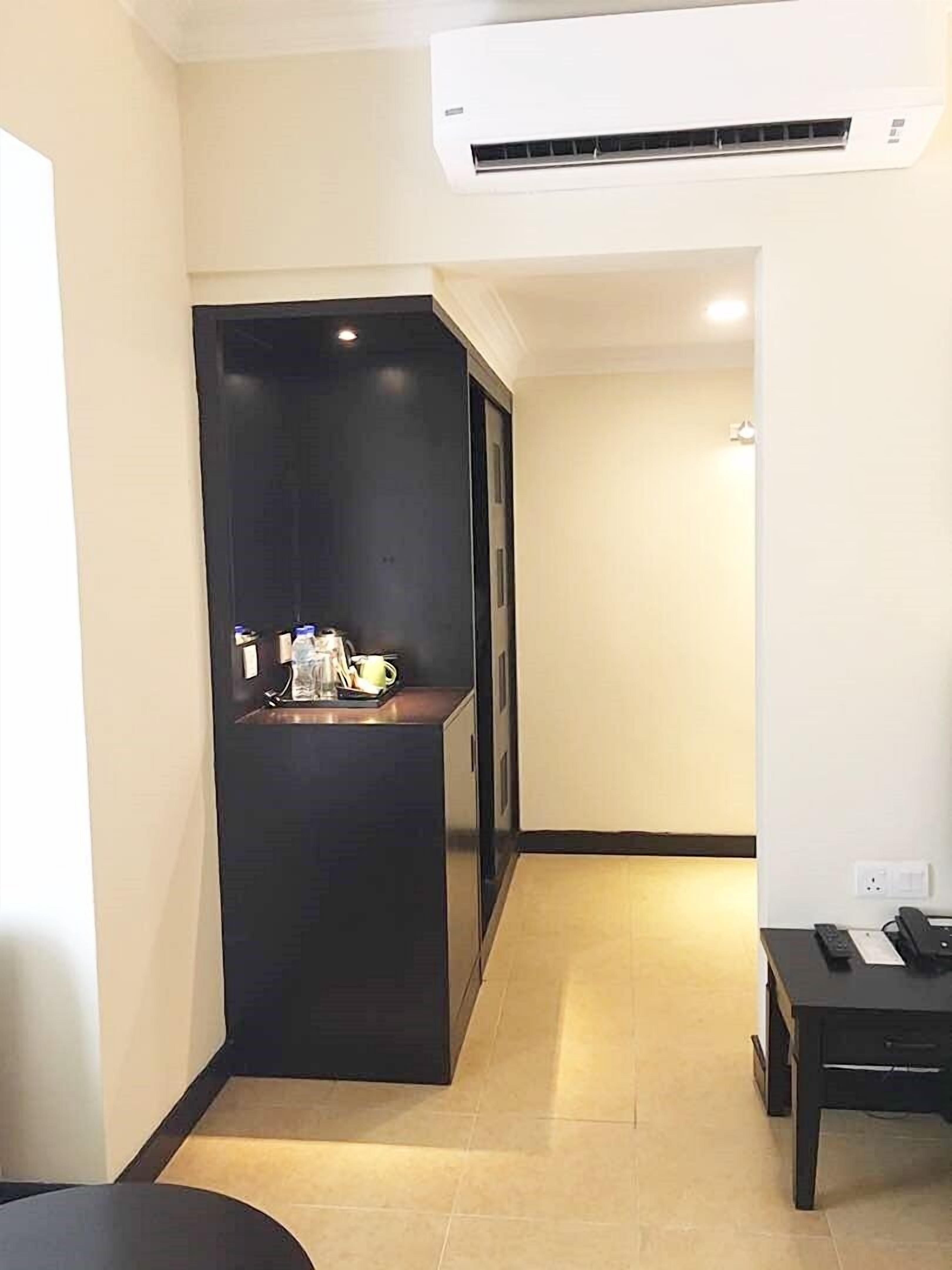 A compact hotel room with a kitchenette, a small table, and an air conditioning unit.