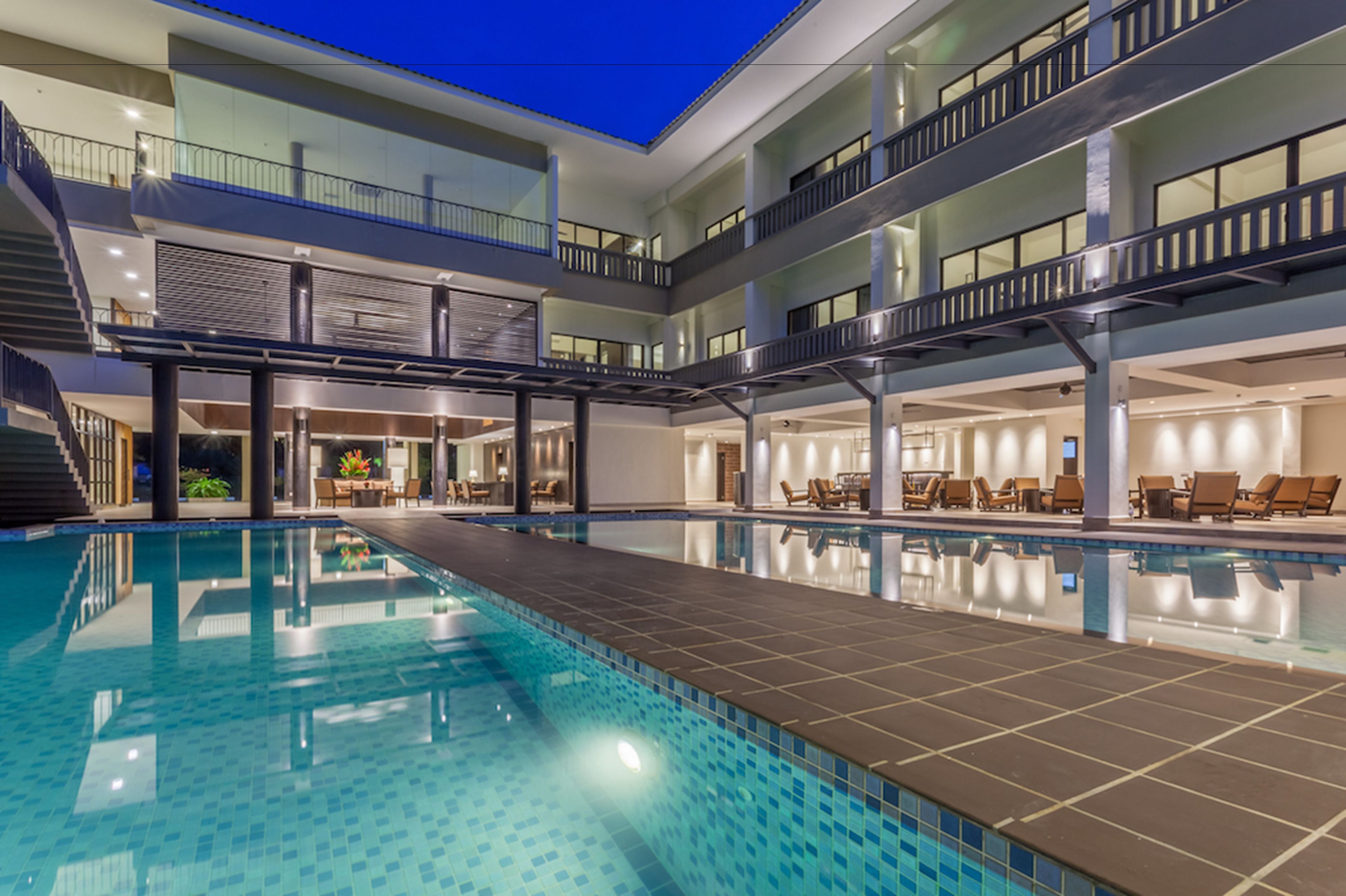 A modern hotel with a large indoor pool, multiple floors, and outdoor seating areas.