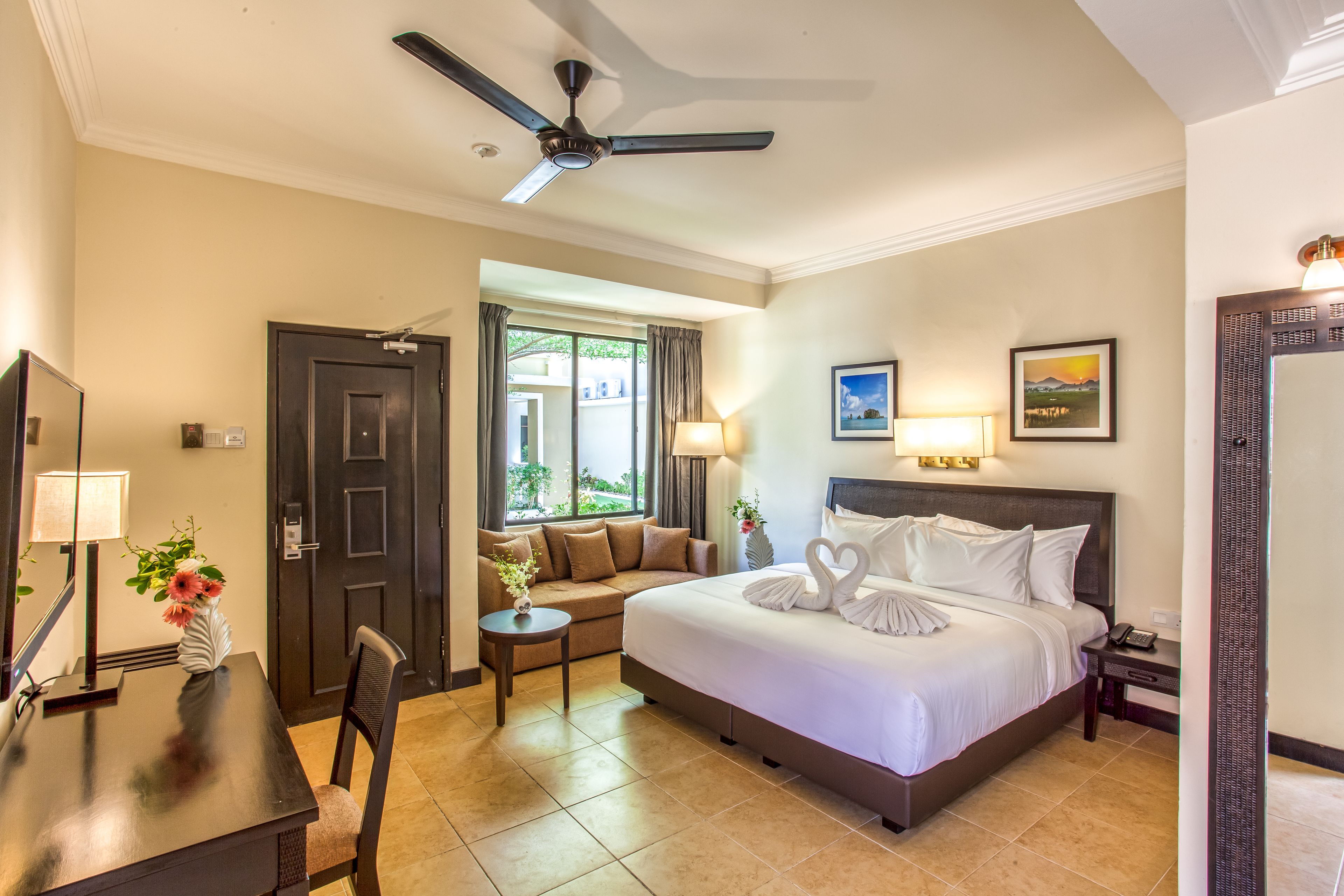 A hotel room with a bed, a desk, a chair, a ceiling fan, and a window with curtains.