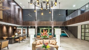 Un lobby amplio con techo alto, un área de estar central con una mesa redonda y una escalera que conduce a un nivel superior.