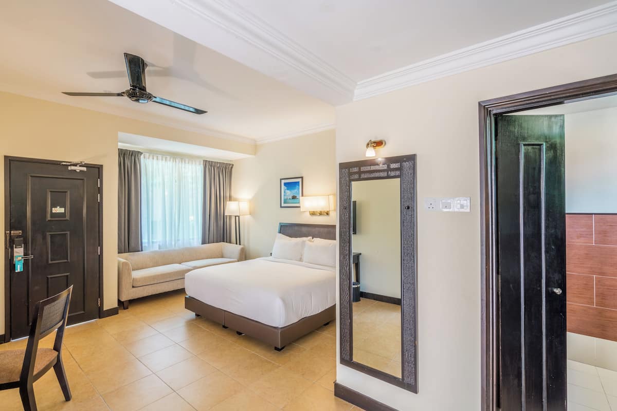 Een hotelkamer met een bed, een stoel, een bureau, een plafondventilator, een raam met gordijnen en een deur.