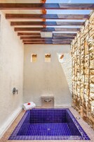 A small, enclosed bathroom with a stone wall, a wooden ceiling, and a blue-tiled floor.