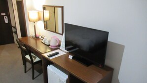 Una habitación de hotel con un escritorio de madera, un televisor, un refrigerador pequeño, una lámpara y un espejo.