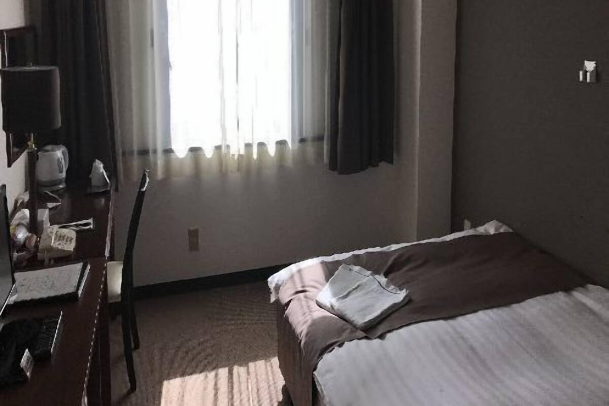 Hotelkamer met een bed, een bureau met stoel, een raam met gordijnen en een airconditioning.