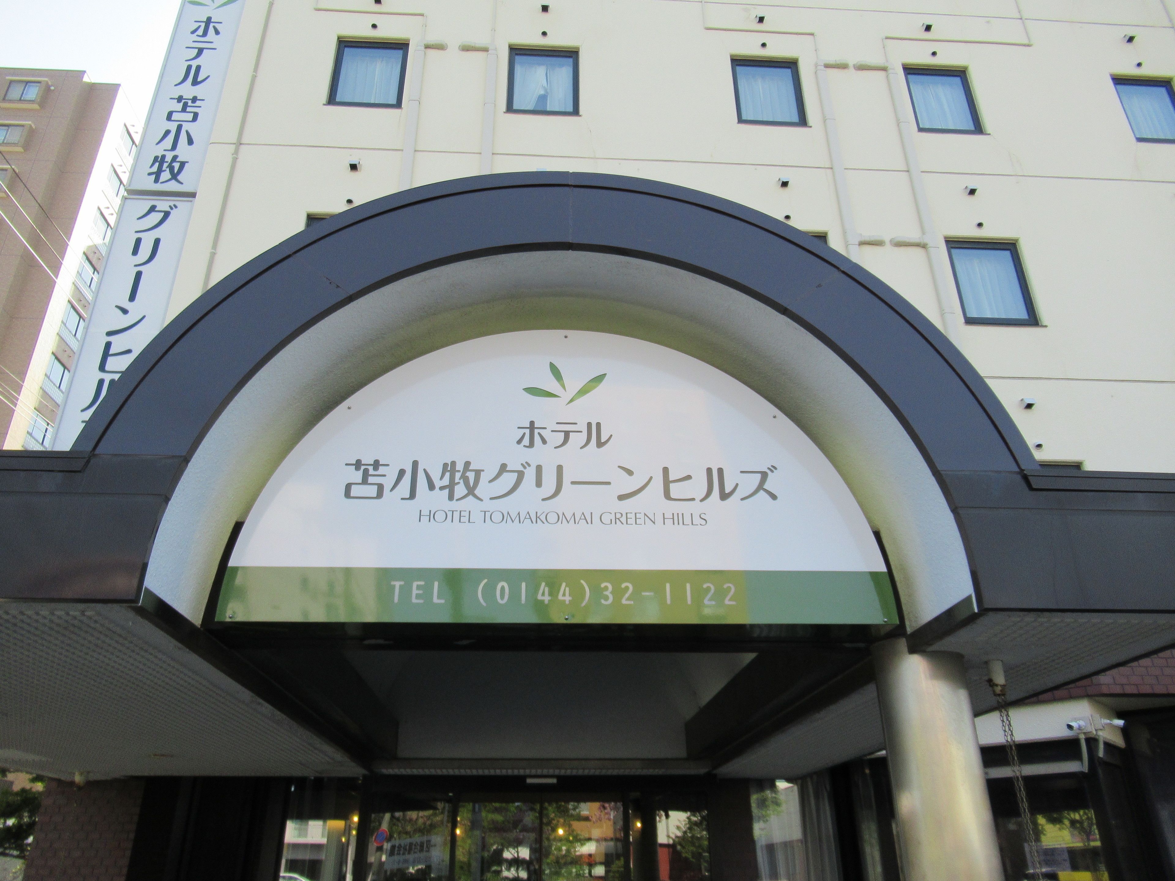 A hotel entrance with a sign displaying the name "Hotel Tomakomai Green Hills" and a telephone number.