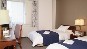 Habitación de hotel con dos camas, un escritorio con lámpara, una silla y una mesita de noche con teléfono.