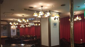 Un interior de restaurante con varias mesas y sillas, luces de techo y una barra.