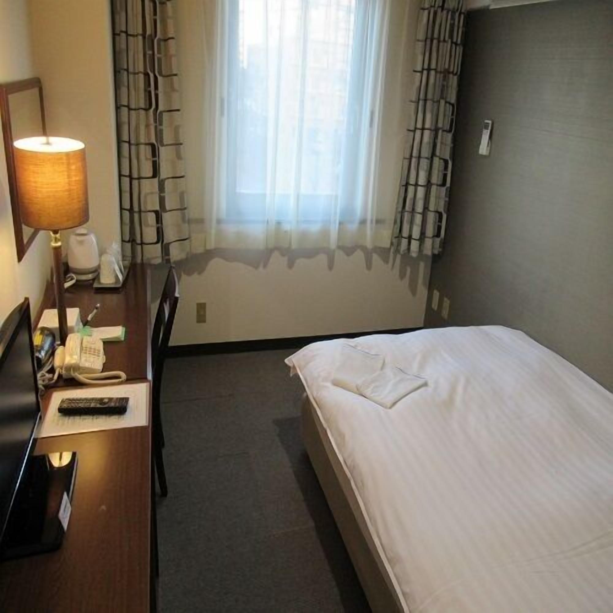 A hotel room with a bed, a desk with a lamp, a telephone, and a chair.