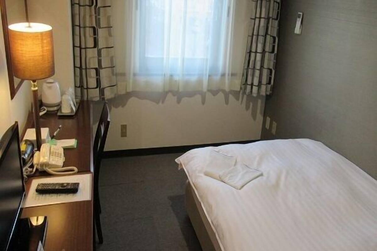 Een hotelkamer met een bed, een bureau met een lamp, een telefoon en een stoel.