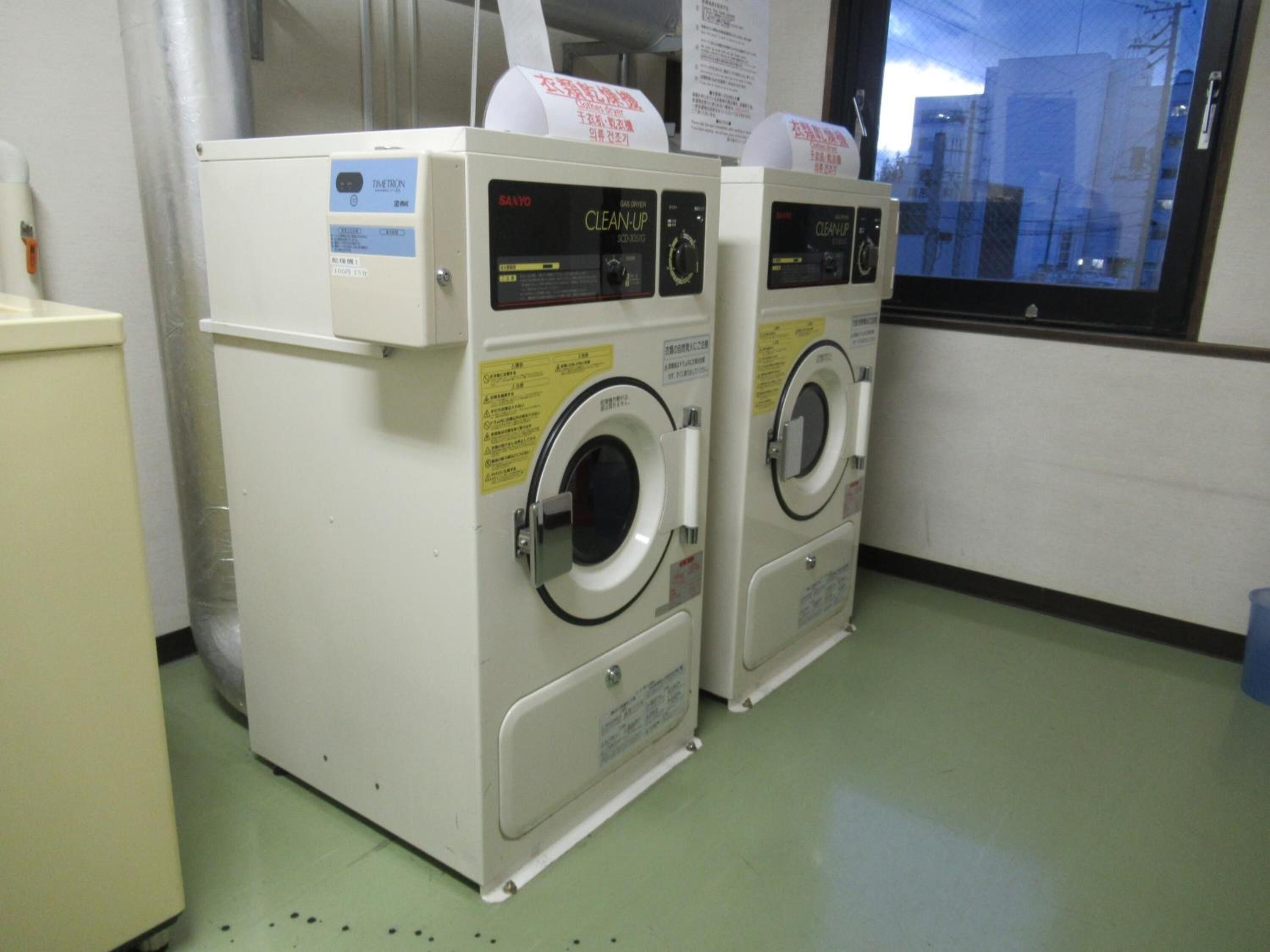 Two front-loading washing machines in a room with a green floor and a window showing a cityscape.