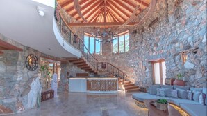 Un intérieur spacieux avec un mur en pierre, un escalier en bois, un comptoir d’accueil et un espace détente.