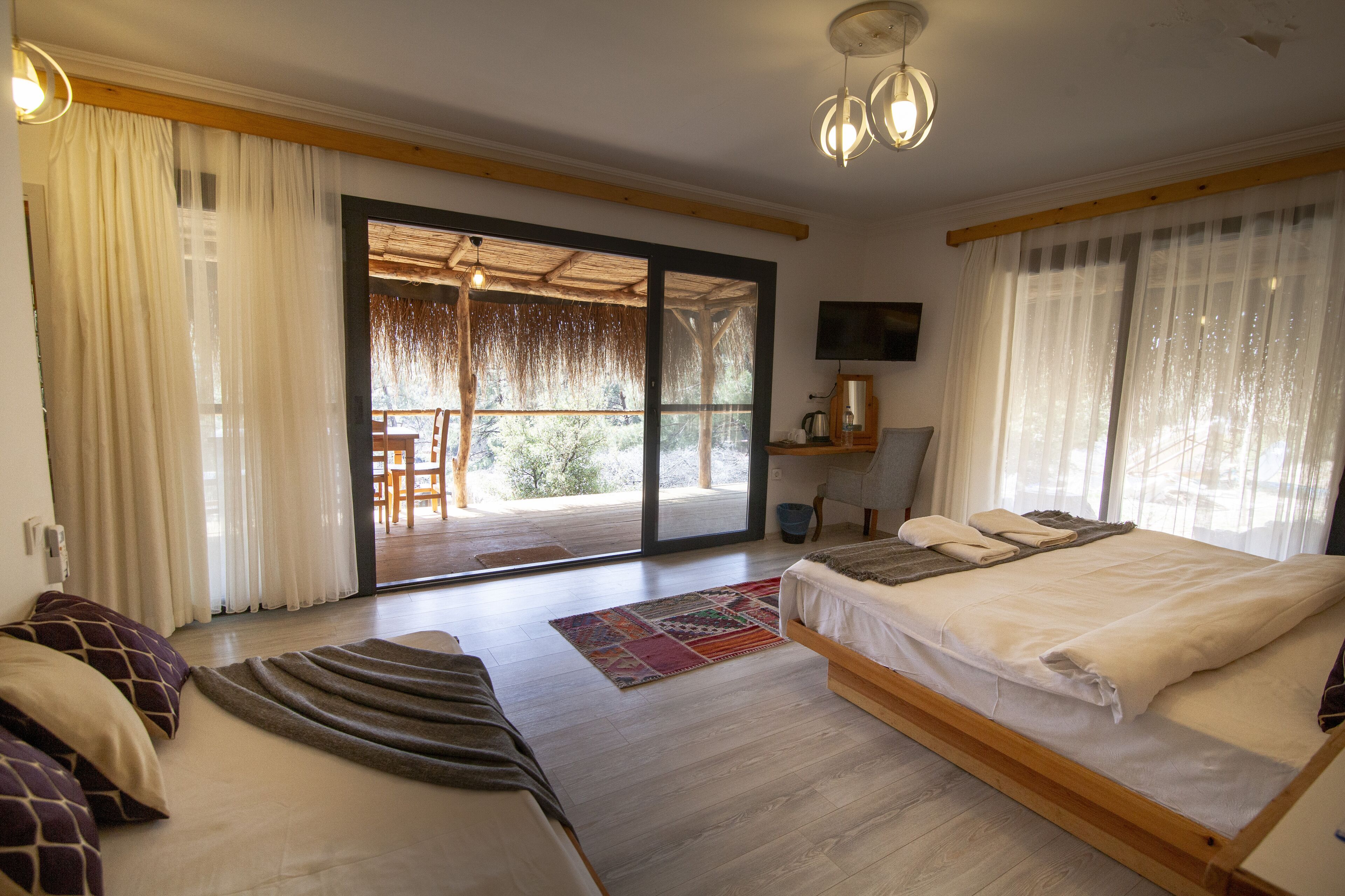 A bedroom with a large bed, a sofa, a TV, and a sliding glass door leading to an outdoor area.