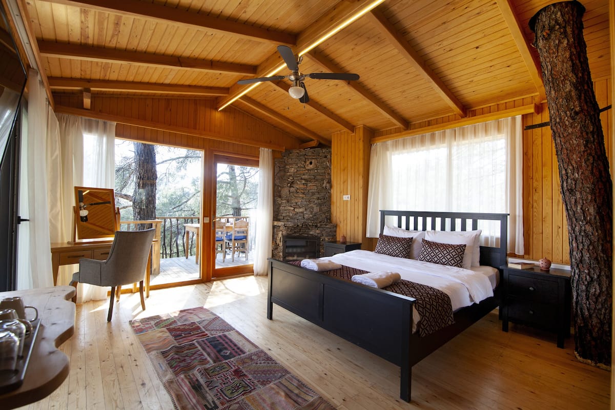 Ein Schlafzimmer einer Holzhütte mit einem Bett, einem Schreibtisch und einem Kamin aus Stein.