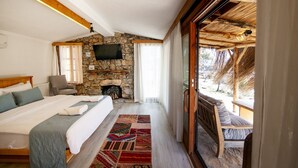 Une chambre avec une cheminée en pierre, un lit recouvert d’une couverture bleue, un téléviseur fixé au mur et une vue sur l’extérieur grâce à une porte vitrée.