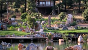 Une cabane dotée d’une terrasse donnant sur un lac, entourée de rochers et de verdure.