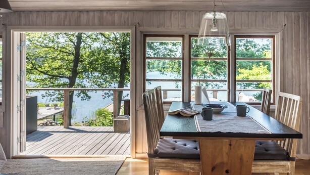 Une table de salle à manger en bois, donnant sur un lac grâce à de grandes fenêtres.