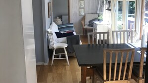 Un coin repas avec une table et des chaises en bois, un canapé blanc et un fauteuil en osier.