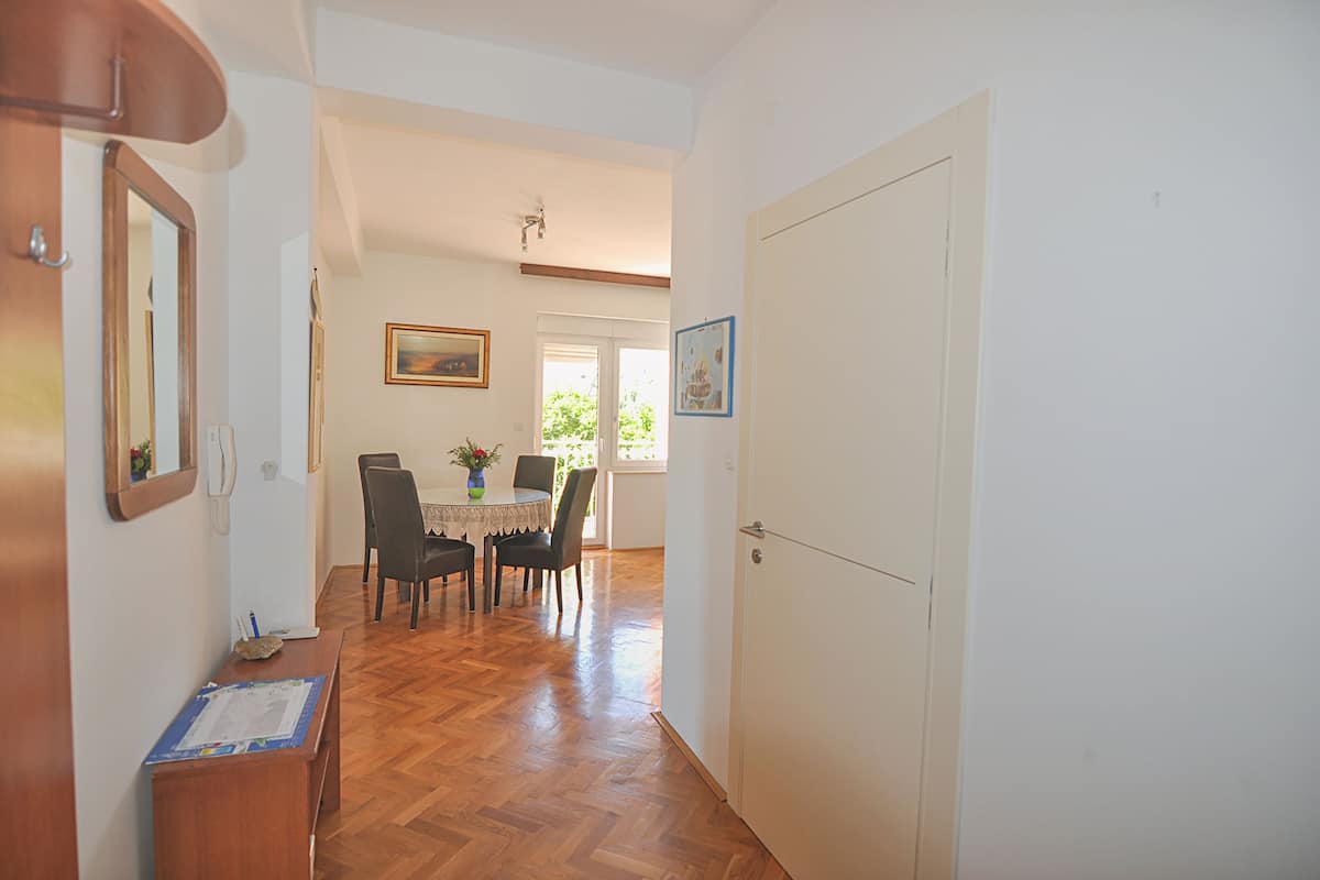 Um corredor com piso de madeira, uma sala de jantar com mesa e cadeiras, e uma porta branca.
