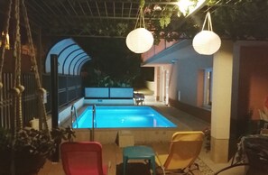 An outdoor swimming pool area with a covered seating area, a small table, and hanging lanterns. - Marjan park (Split)