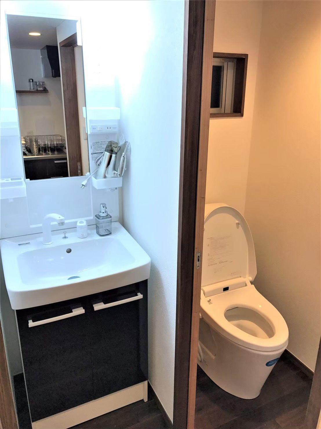 A bathroom with a white sink, dark cabinet, and a white toilet.