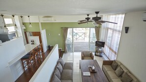 A spacious living area with a sofa set, a dining table, and a TV. There is a balcony with a view. - T&T Vacation Rentals (Onna)
