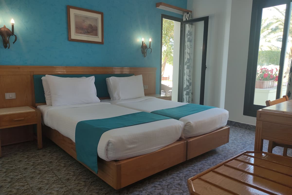 A double bed with a wooden headboard, two bedside tables, a teal bedspread, and a framed picture on the wall.