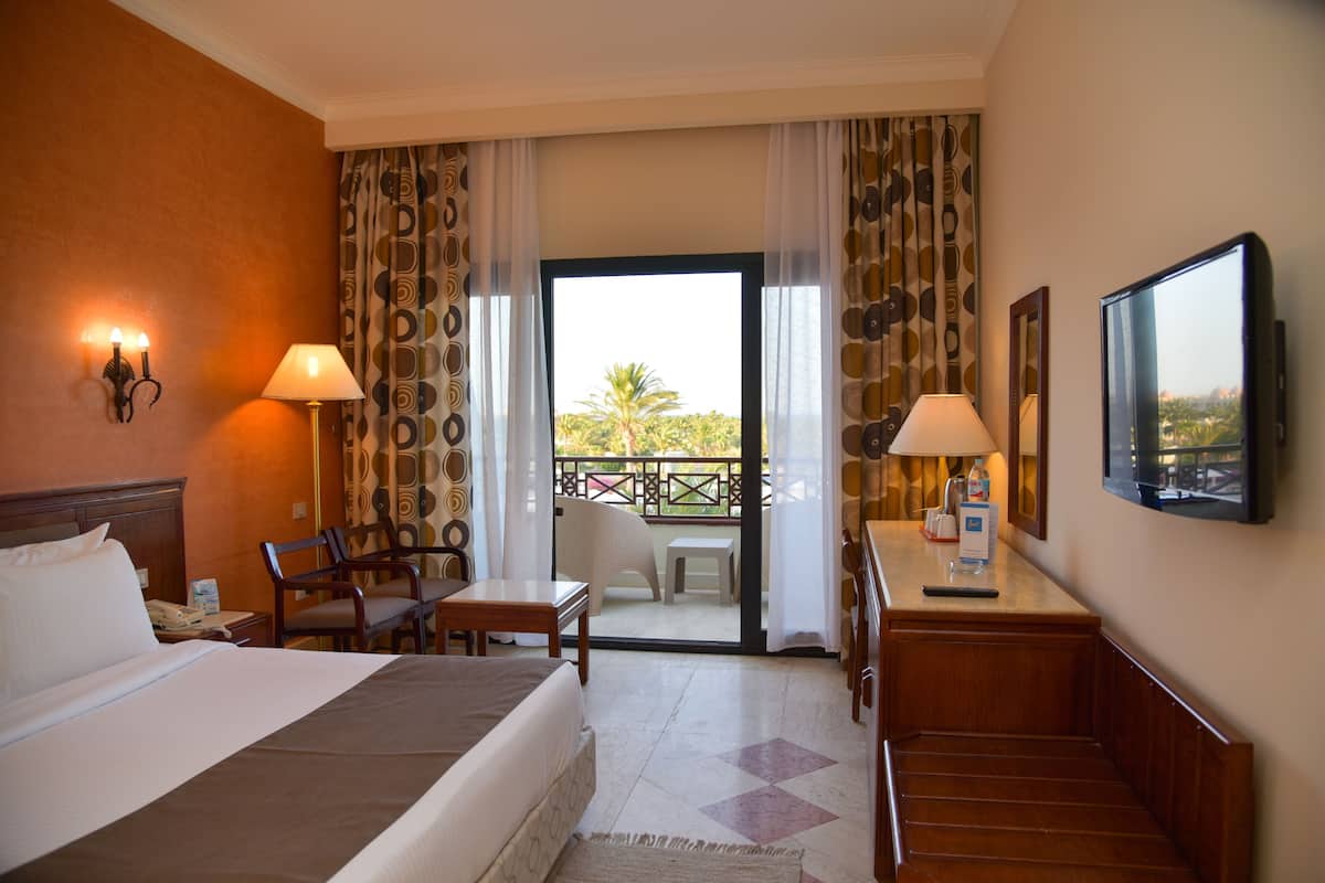 A hotel room with a bed, two chairs, a desk, a TV, and a balcony with a view.