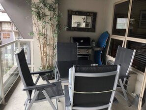 Un balcon avec une table, des chaises, un barbecue et un pot de fleurs.
