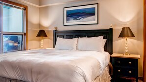 Een net opgemaakt bed met witte lakens, twee bedlampjes, een lijst met kunstwerk erboven en een raam aan de linkerkant.