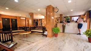 A hotel lobby with a reception desk, wooden benches, a marble floor, and a clock on the ceiling. - Ranthambhore National Resort (Sawai Madhopur)