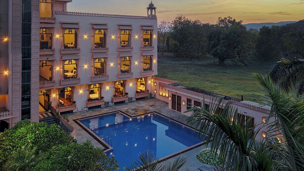 A multi-story building with a swimming pool, balconies with lights, and a view of the surrounding landscape. - Ranthambhore National Resort (Sawai Madhopur)