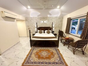 A bedroom with a bed, a stone wall, a window with curtains, a chair, and a small table. - Ranthambhore National Resort (Sawai Madhopur)