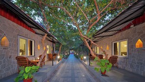 A corridor with stone walls, wooden furniture, and potted plants. - Ranthambhore National Resort (Sawai Madhopur)