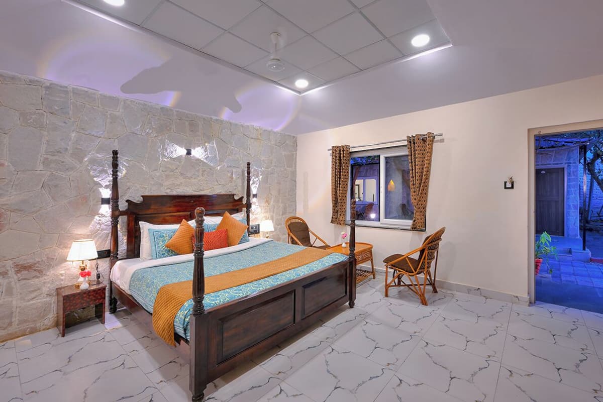 Une chambre avec un mur en pierre, un lit en bois, une fenêtre ornée de rideaux à motifs et une vue sur un espace extérieur.