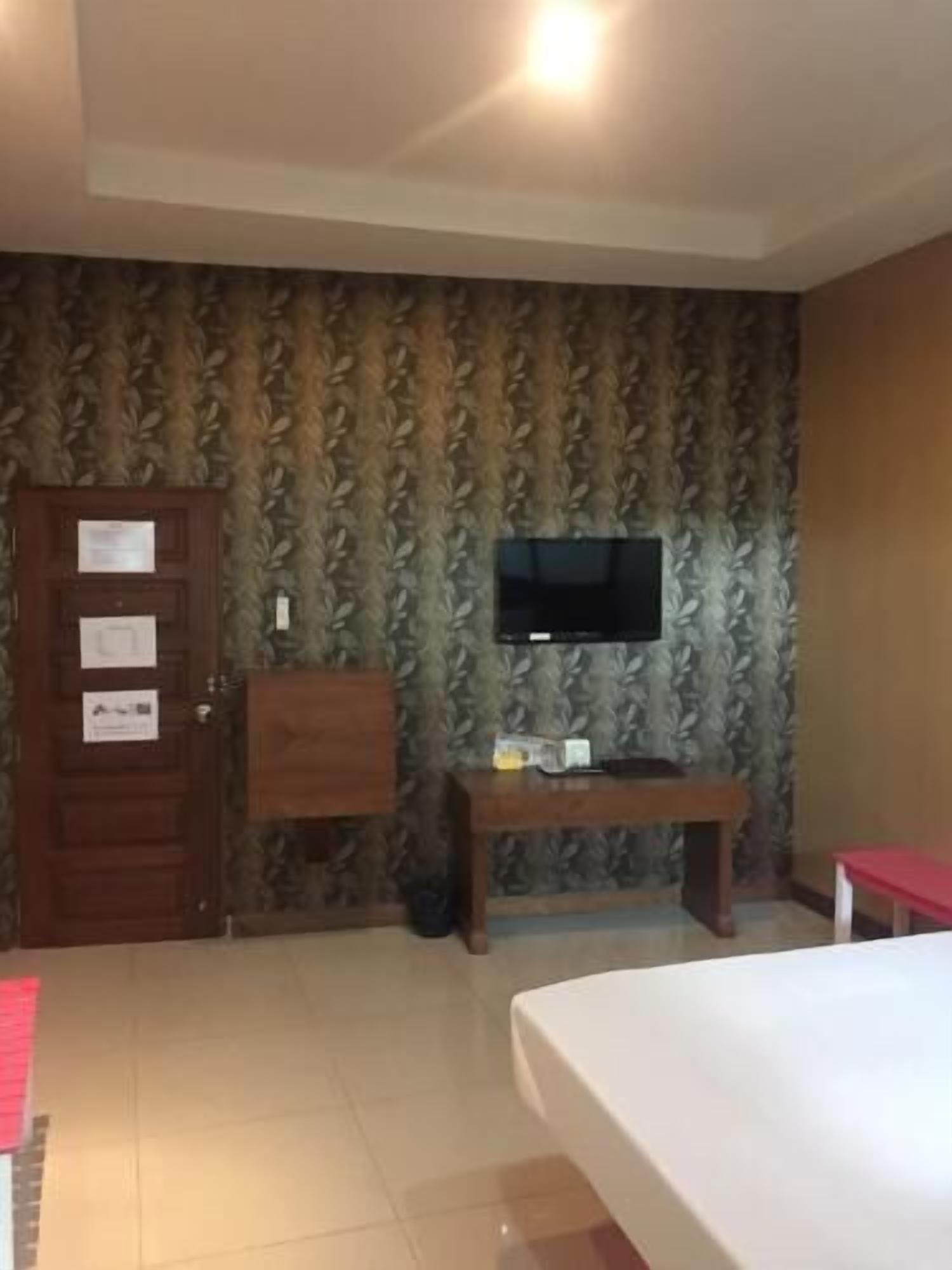 A hotel room with a bed, a television mounted on the wall, a wooden cabinet, and a bench.