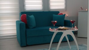 A living room with a teal sofa, a small white table with candles, and a blue rug. - Suw Hotel (Atakum)
