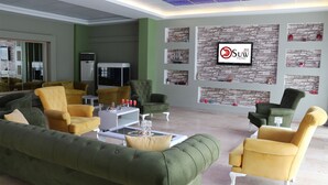 A modern lounge area with green and yellow upholstered sofas, a white coffee table, and a television mounted on a stone-textured wall. - Suw Hotel (Atakum)