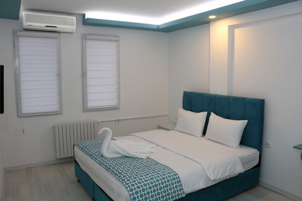 A bedroom with a bed, a radiator, and two windows with blinds.