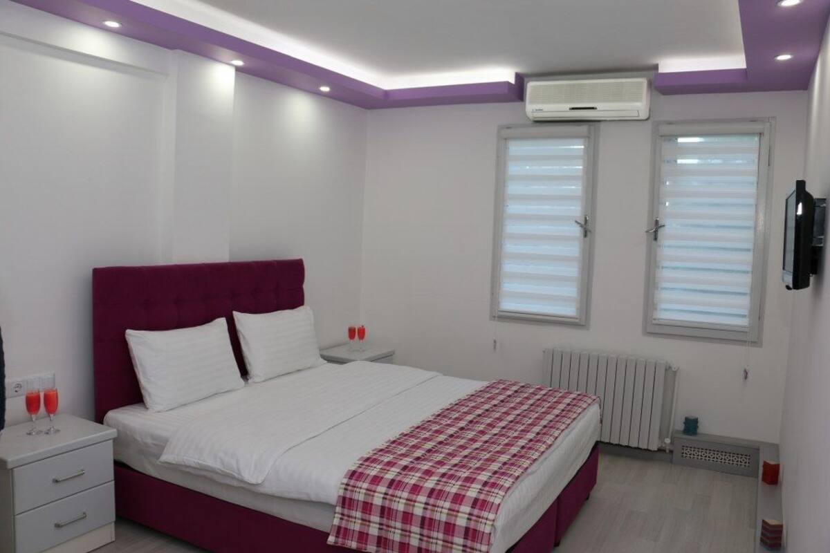 Ein Schlafzimmer mit Bett, Nachttischen, Heizkörper und einem Fenster mit Jalousien.