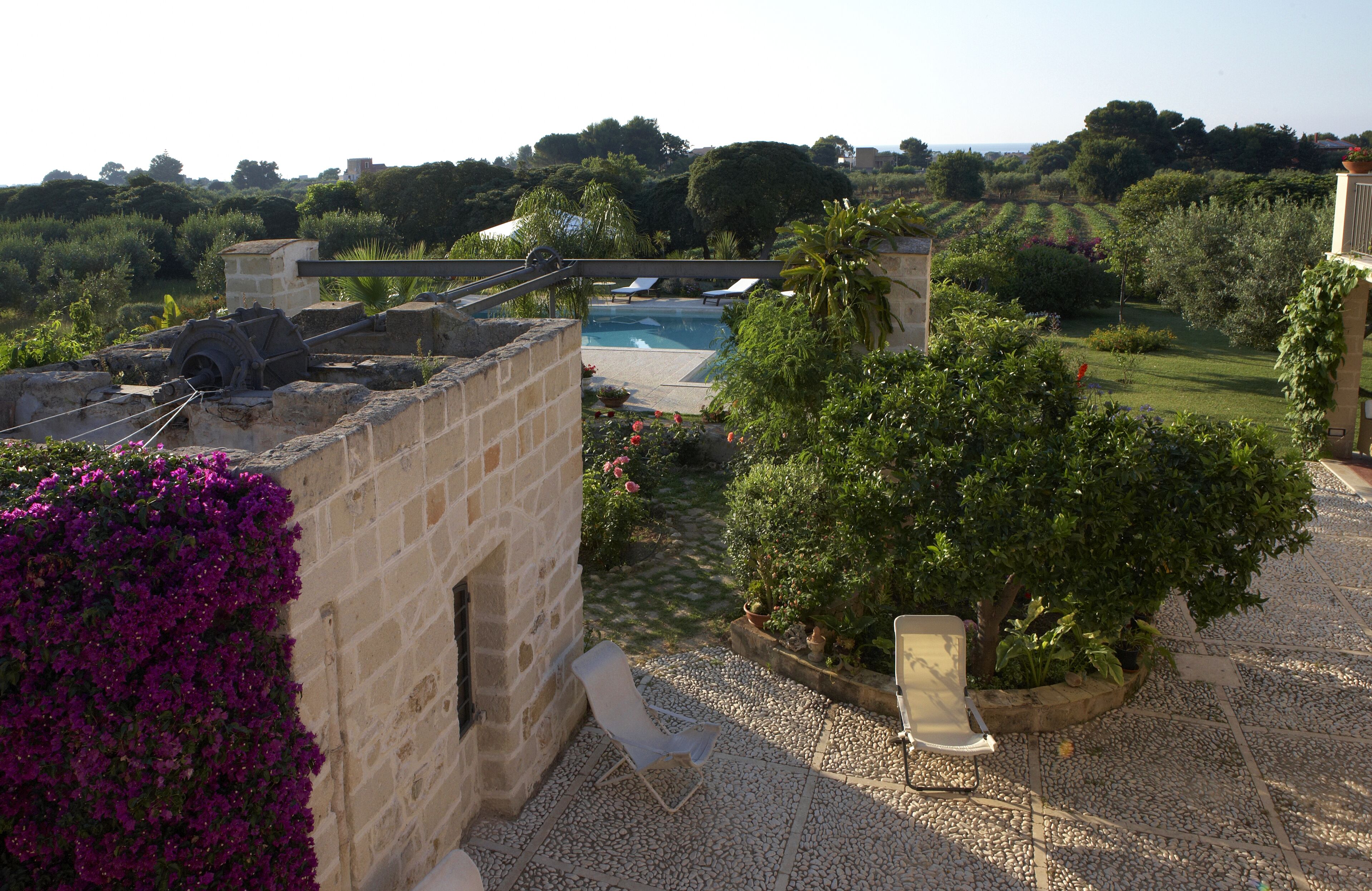 Zona de piscina en la azotea con un muro de piedra, una silla y un jardín con un árbol y flores.