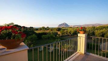 A balcony with a view of a landscaped garden and distant mountains.