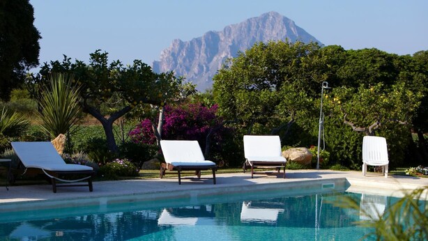 Una piscina con sillas de descanso y una montaña al fondo.