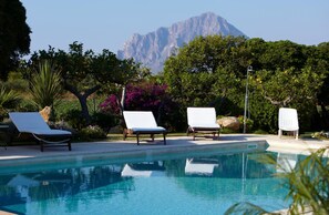 A pool with lounge chairs and a mountain in the background. - Baglio Sant'Andrea (Valderice)