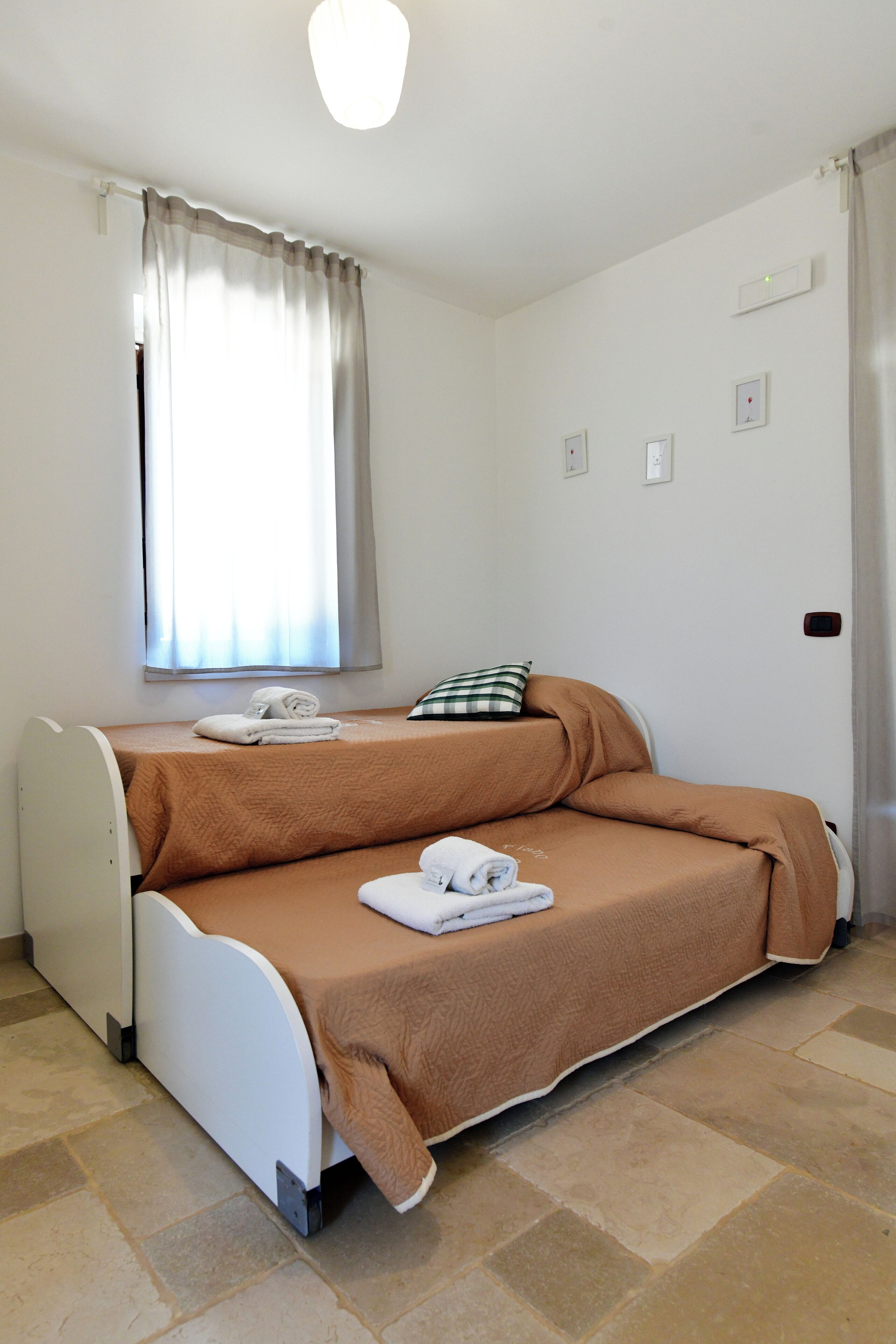 Une petite pièce comprenant un lit, une fenêtre avec des rideaux, un luminaire fixé au mur et une prise de courant.