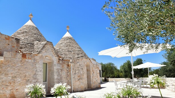 A stone building with conical roofs, outdoor seating, and white flowers.