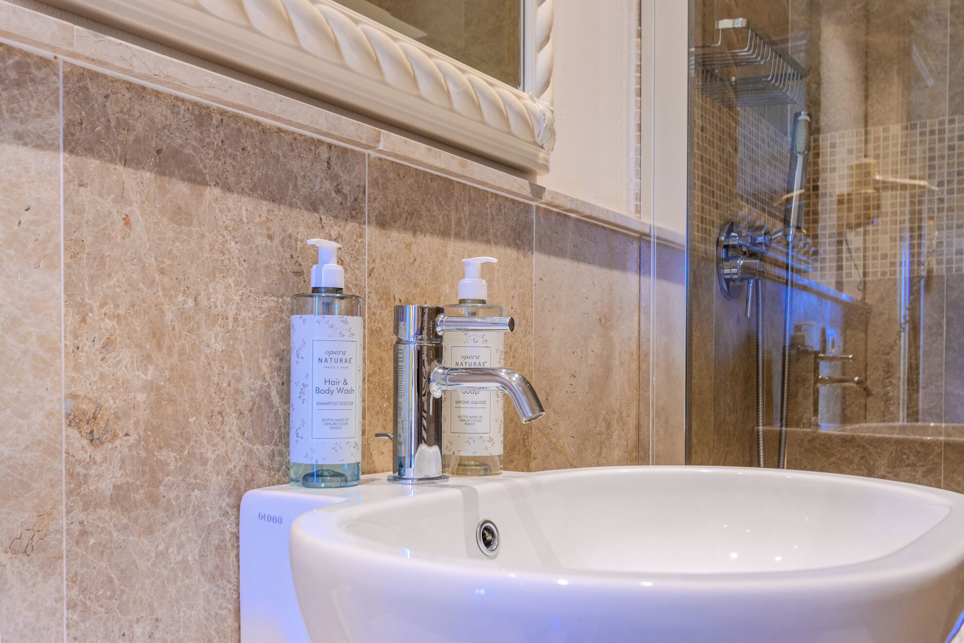 Et badeværelse med en hvid vask, to flasker shampoo og sæbe, samt et bruseområde.